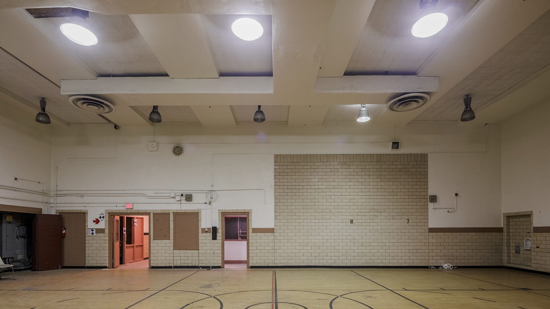 Wide-shot photo of a gym. Three lights are on the ceiling and there are three doors on the left side of the room.