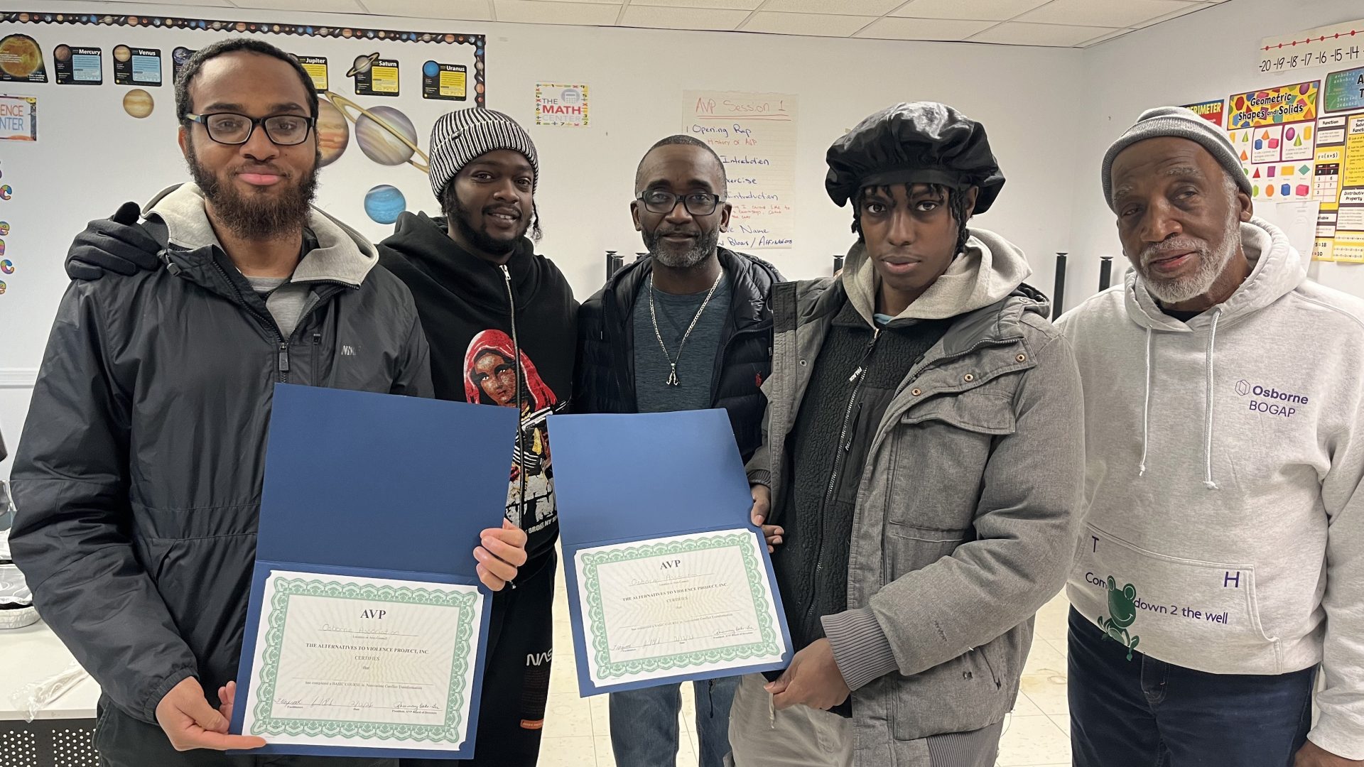 3 participants stand in a classroom with two Osborne staff holding their certificates. They all smile at the camera.